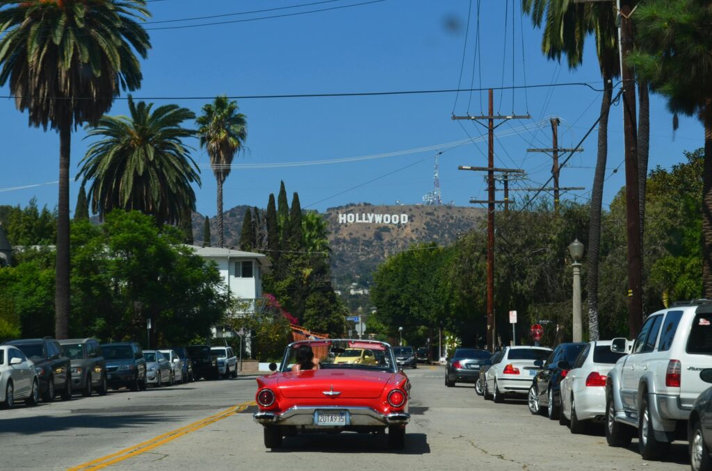 pexels-photo-1688186-1688186 Red convertible driving down a sunny street towards the iconic Hollywood sign in Los Angeles.